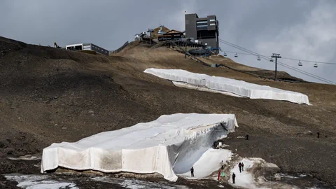 Berggipfel mit Gebäuden, Seilbahn und schneebedeckten Flächen.